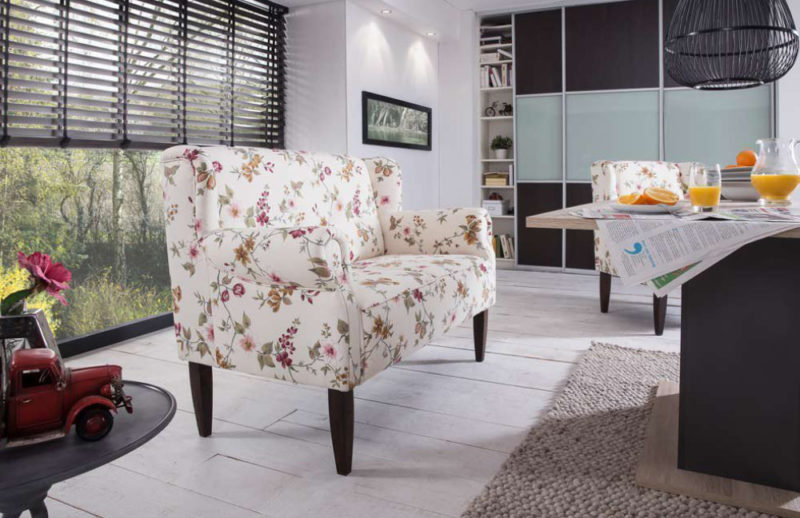 Helles Küchensofa im Landhausstil mit Blumen und Holzbeinen steht in einer modernen Einrichtung.